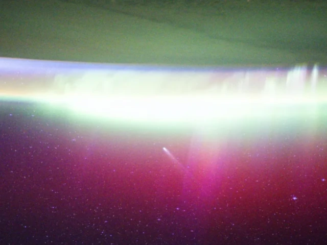A bright, neon-like aurora radiates above Earth, seemingly absorbing Comet Lemmon (C/2025 A6) as it soars past the planet at a distance of about 57.2 million miles (92.1 million kilometers) in October 2025.