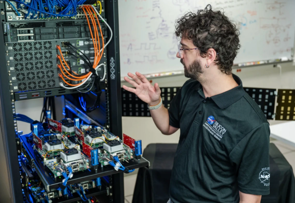 Caleb Adams, Distributed Spacecraft Autonomy project manager, monitors testing alongside the test racks containing 100 spacecraft computers at NASA’s Ames Research Center in California.