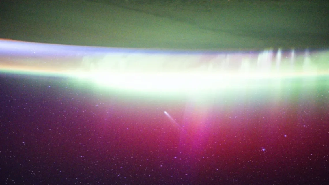 A bright, neon-like aurora radiates above Earth, seemingly absorbing Comet Lemmon (C/2025 A6) as it soars past the planet at a distance of about 57.2 million miles (92.1 million kilometers) in October 2025.